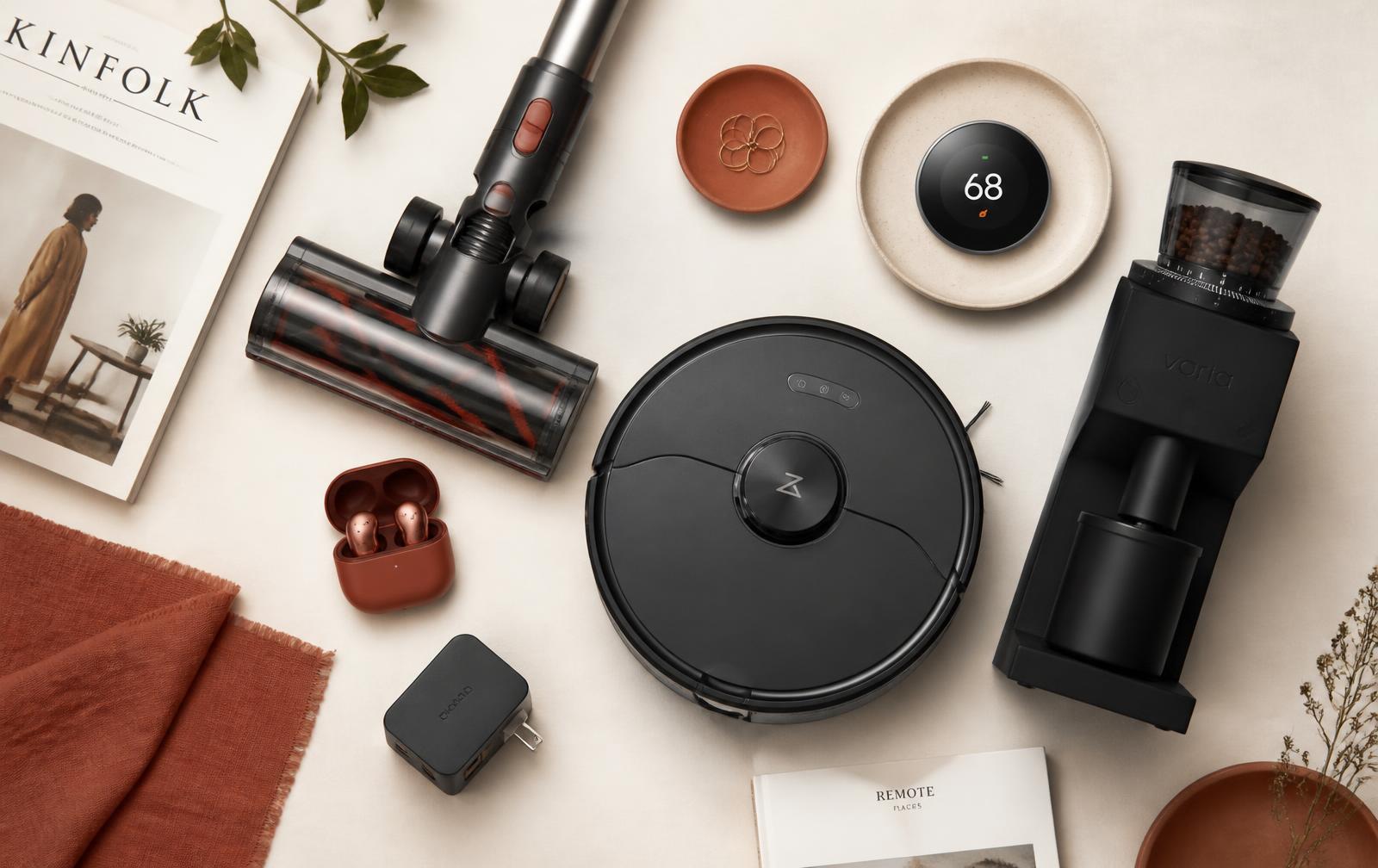 Flat lay of consumer gear including a cordless vacuum, robot vacuum, earbuds and a smart thermostat